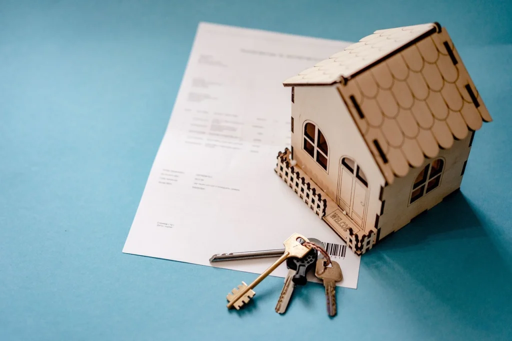 Contrato inmobiliario con llaves y maqueta de casa sobre fondo azul representando acuerdo de venta